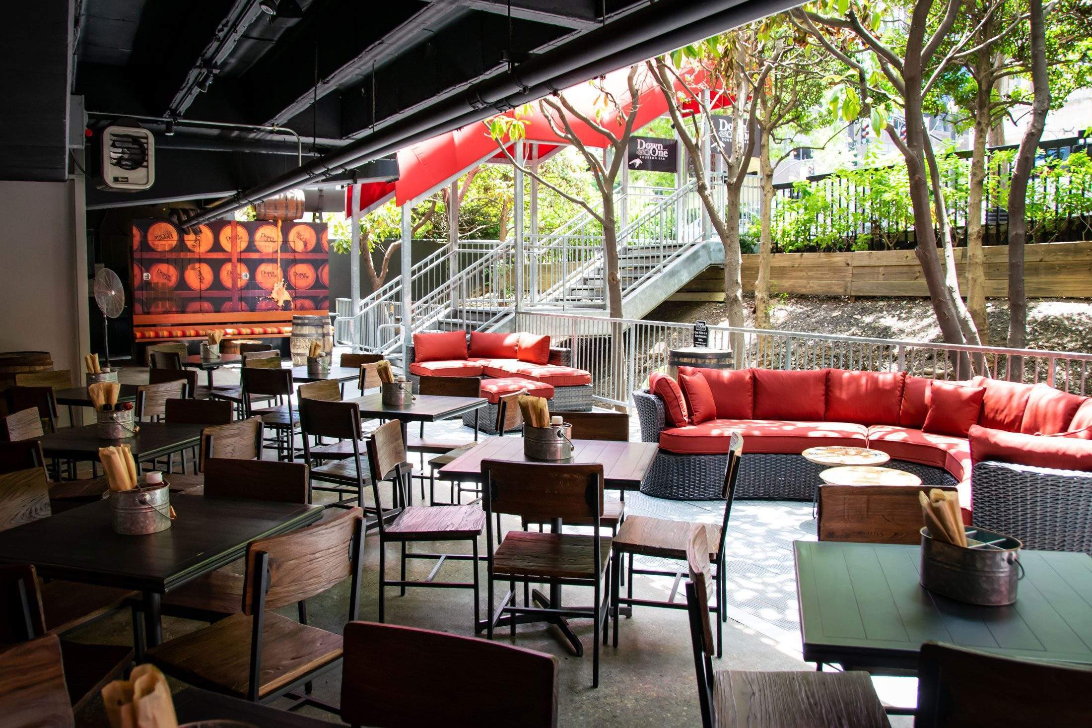 Outdoor lounge with red cushions, tables, chairs, and trees.
