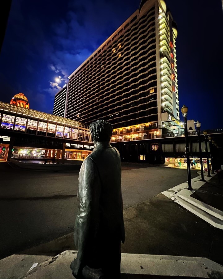 Bronze statue facing large illuminated hotel.